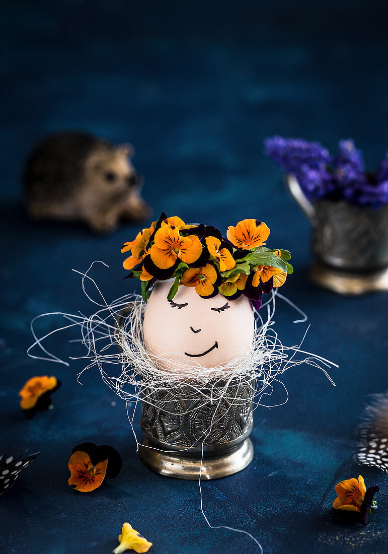An Easter egg with a face and pansies