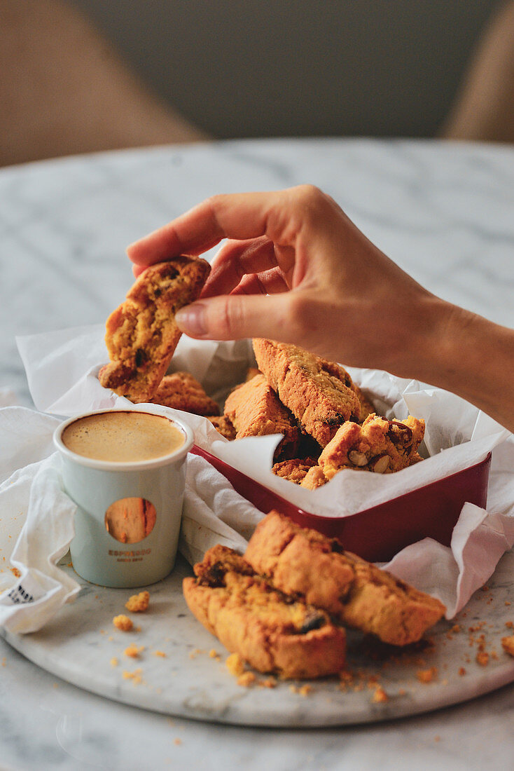 Hand taucht Mandel-Cantuccini in Tasse Kaffee