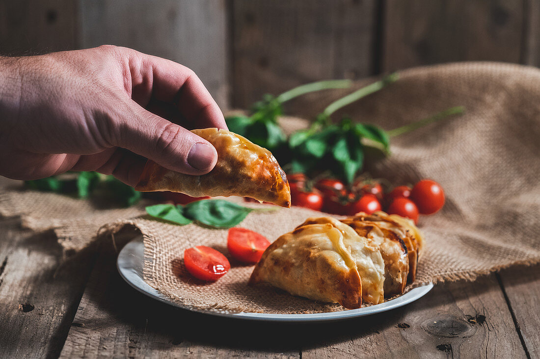 Traditional Spanish homemade turnovers served in dish on rustic wooden table with fresh spinach and tomatoes