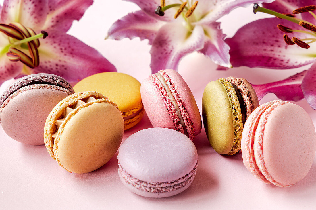 Assorted delectable macarons placed on pink table with fresh lily flowers