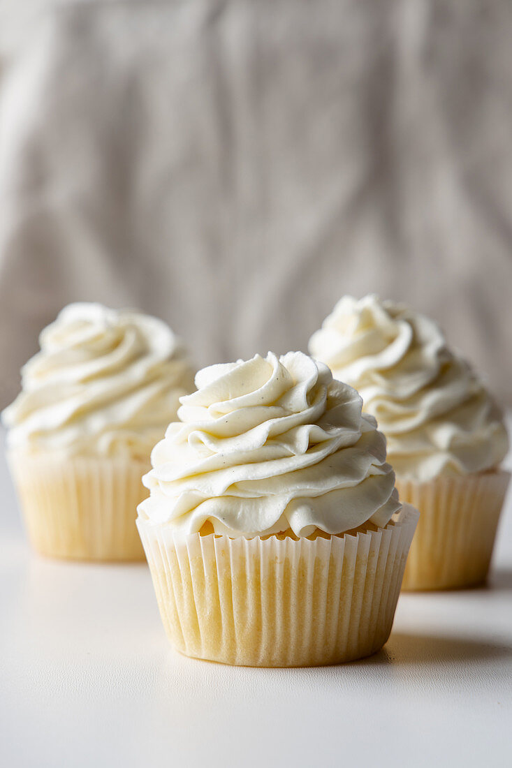 Tasty vanilla cupcakes with sweet cream placed on tray on table on white background