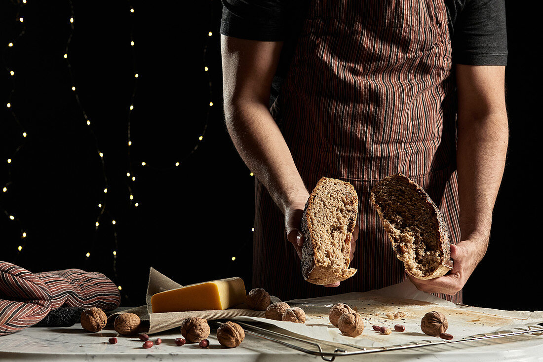 Crop unrecognizable male baker in apron cutting loaf of fresh artisan rye bread with grains