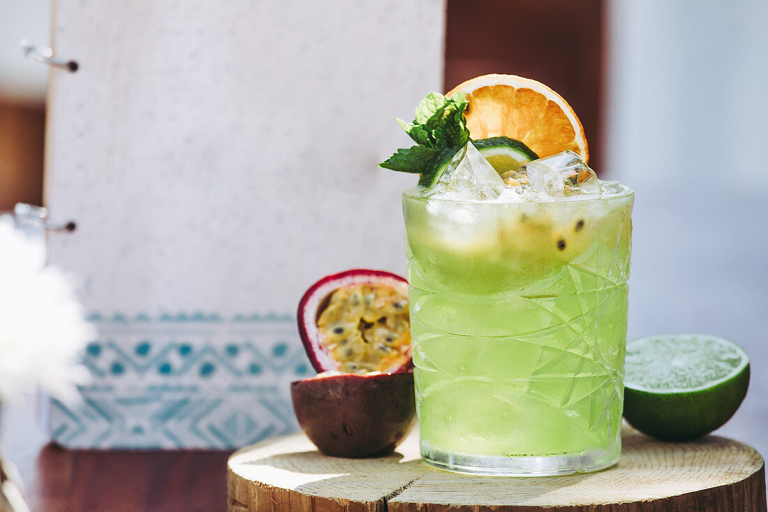 Glass of cold green alcohol Mojito cocktail with fresh passion fruit and lime garnished with mint leaves and fruit slices