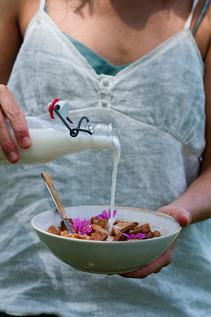 Unrecognizable female adding fresh milk in bowl with cinnamon cereal while preparing healthy breakfast