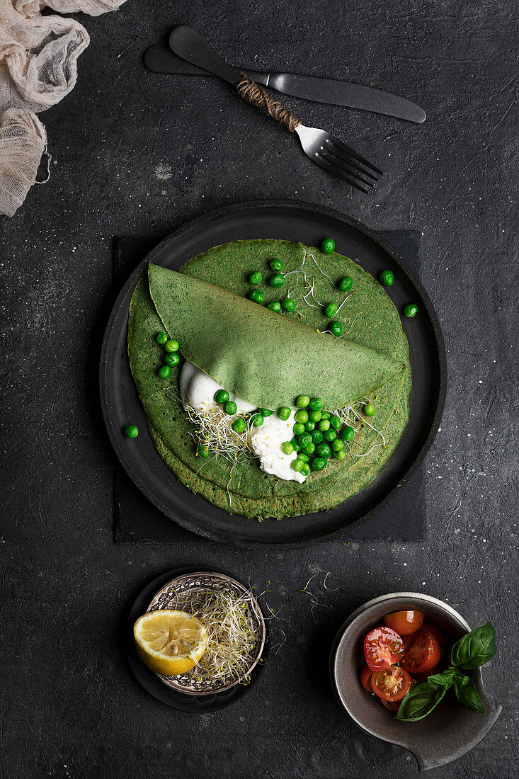 Erbsencrepes mit Sprossen und Sauerrahm auf schwarzem Teller