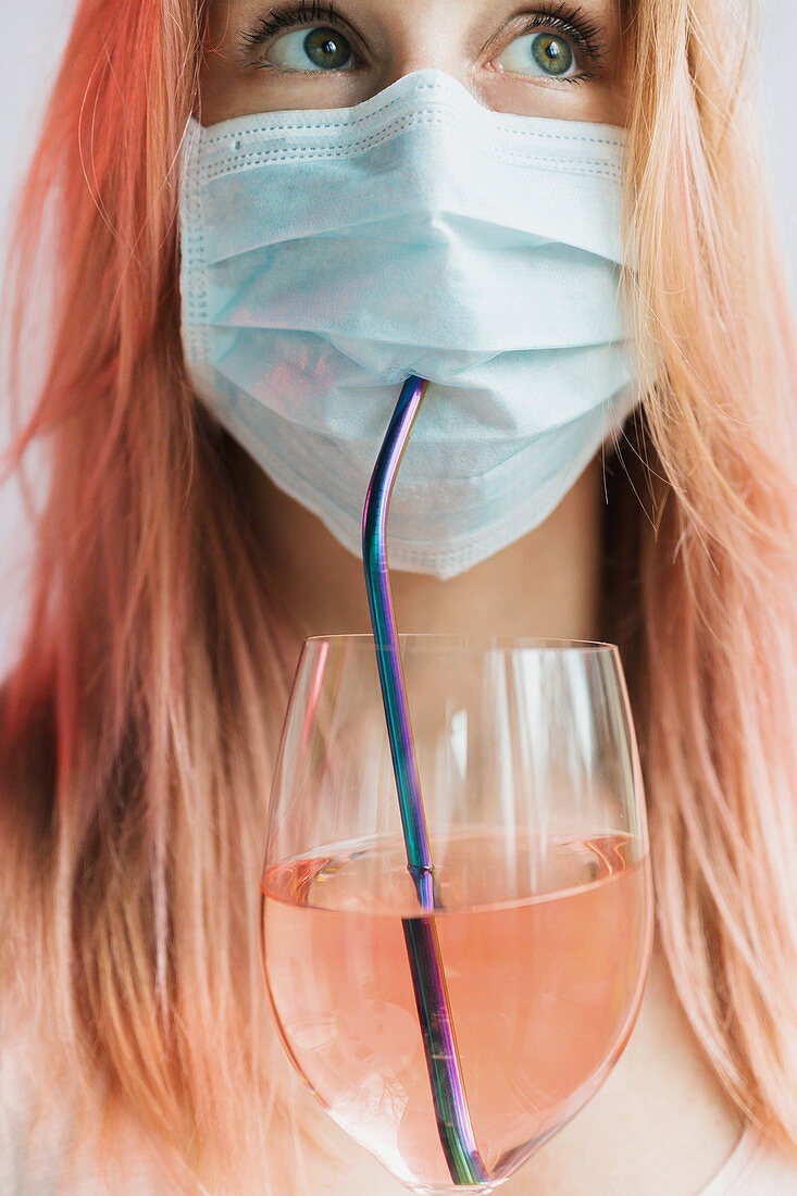 Woman drinking rose wine through straw while wearing face mask