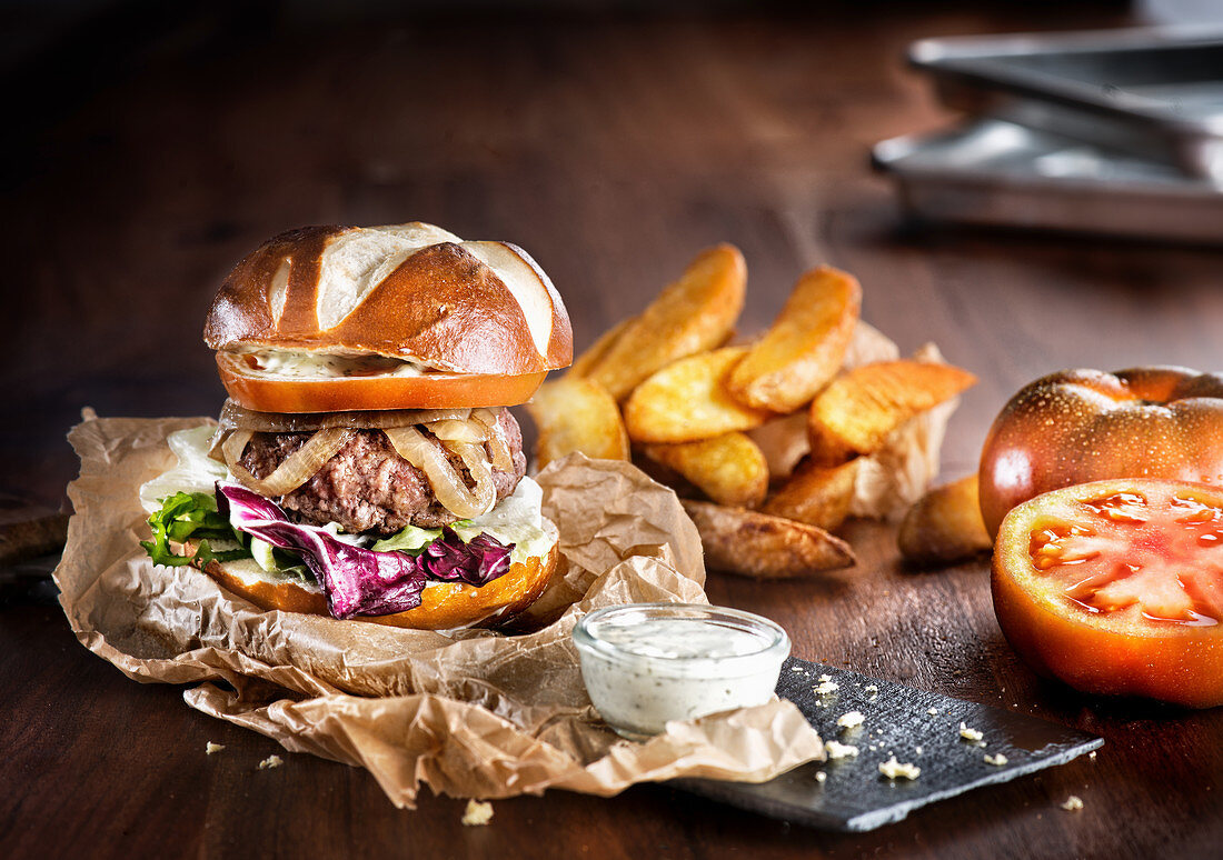 Appetizing big burger with fresh vegetables and beef patty with fried potatoes served on slate board with fries