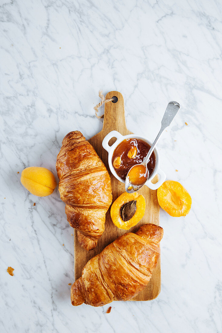 Appetizing fresh croissant served with pot of homemade apricot jam on wooden cutting board