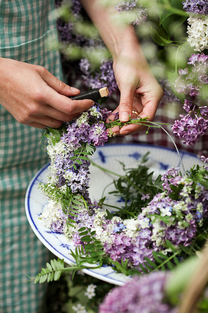 Woman tying wreath of lilac florets and tufted vetch