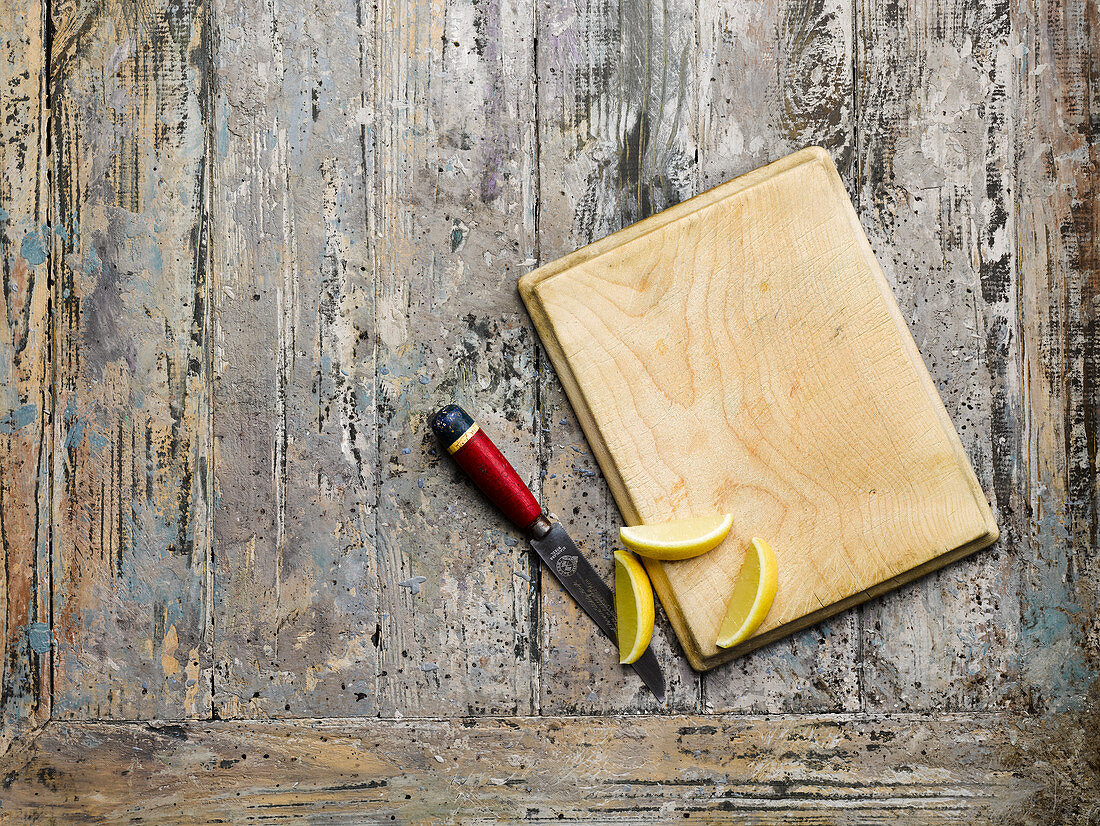 A wooden board, a knife and lemon wedges on a wooden surface