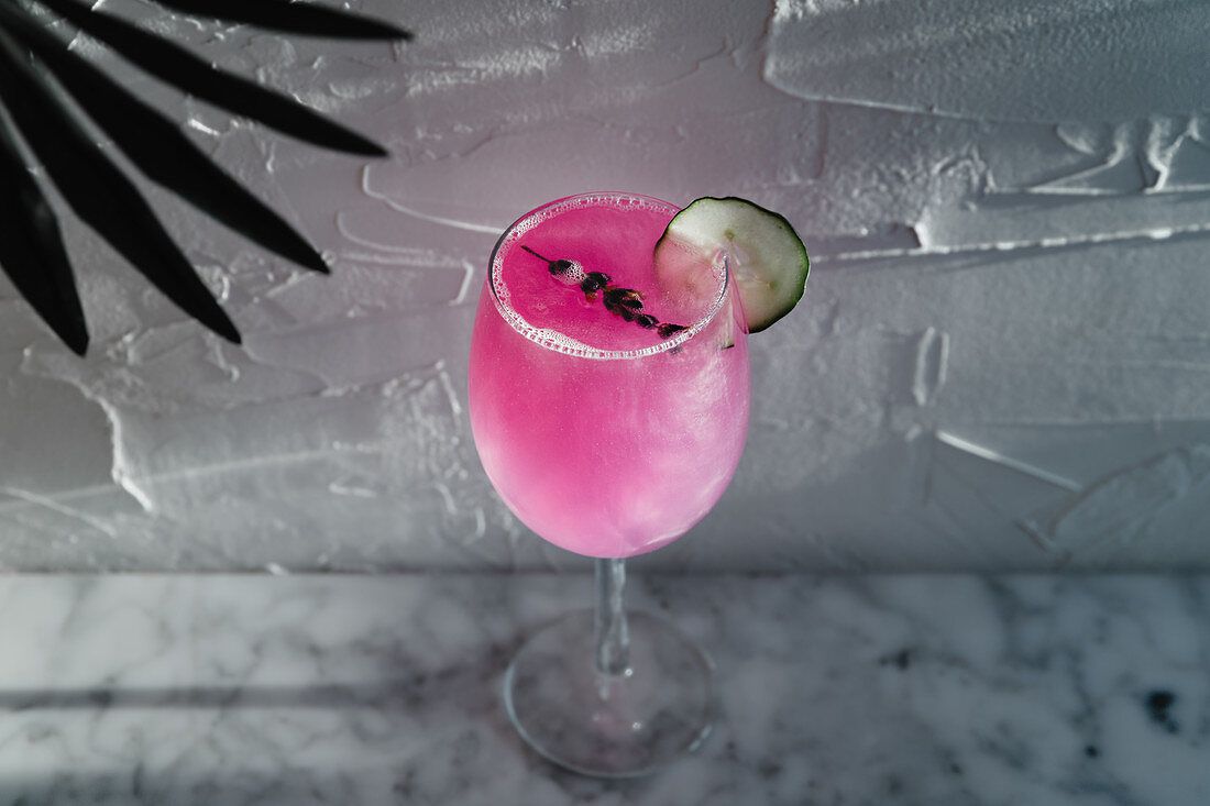 Purple cocktail garnished with herbs and sliced lime