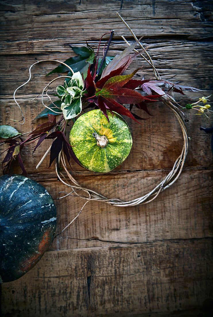 Zierkürbisse und Herbstlaub auf rustikalem Holzuntergrund