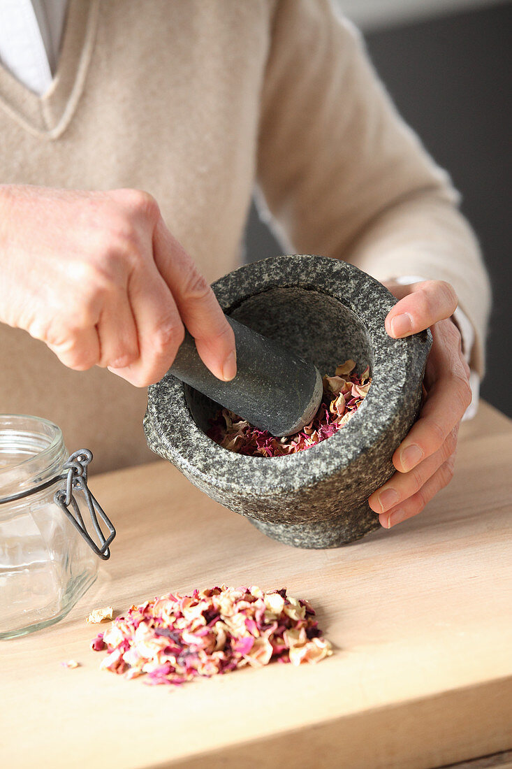 Crushing dried rose petals in a mortar