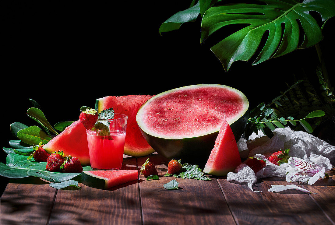 Glass of sweet fruit juice with mint on wooden table with strawberries and ripe watermelon