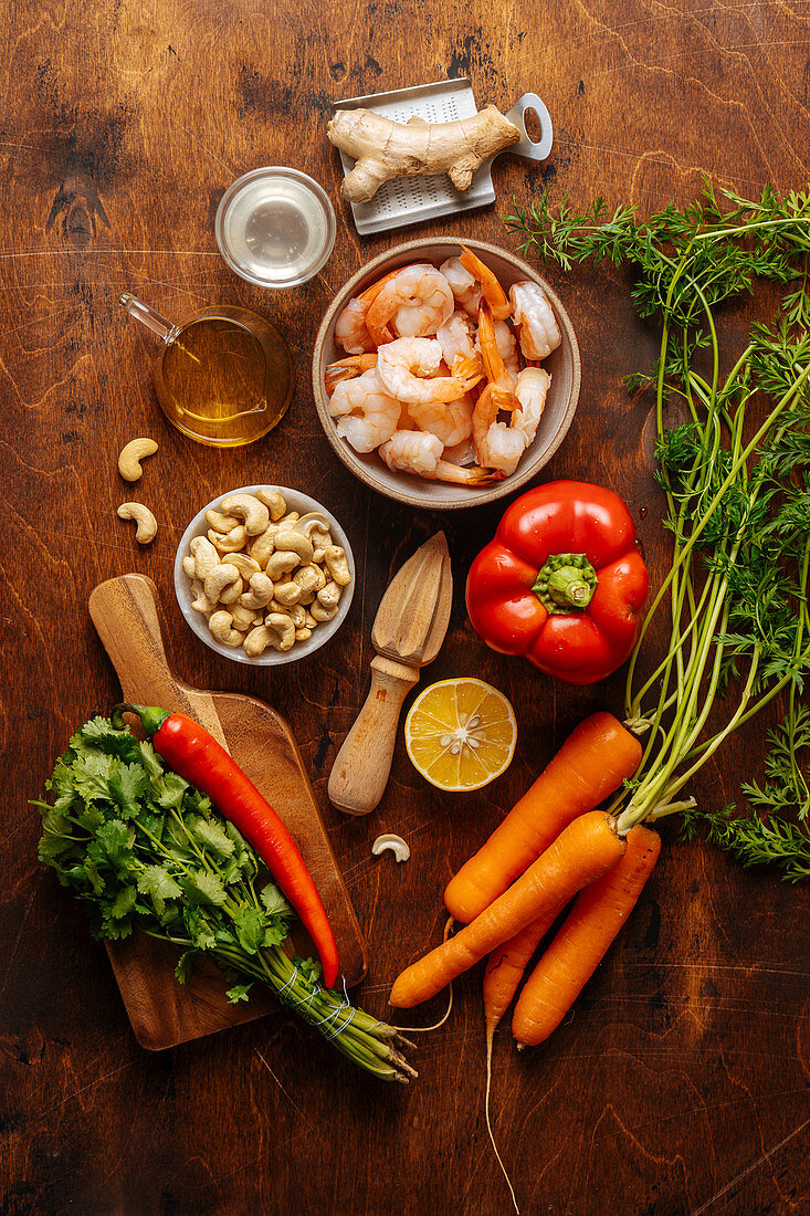 Vegetables and herbs placed near juicer and boiled shrimps on wooden table