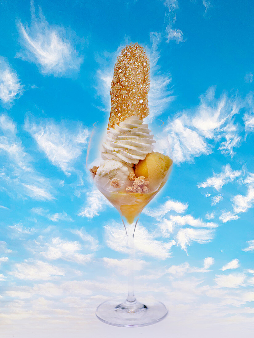 Fruit ice cream with a wafer and whipped cream in front of a cloudy sky