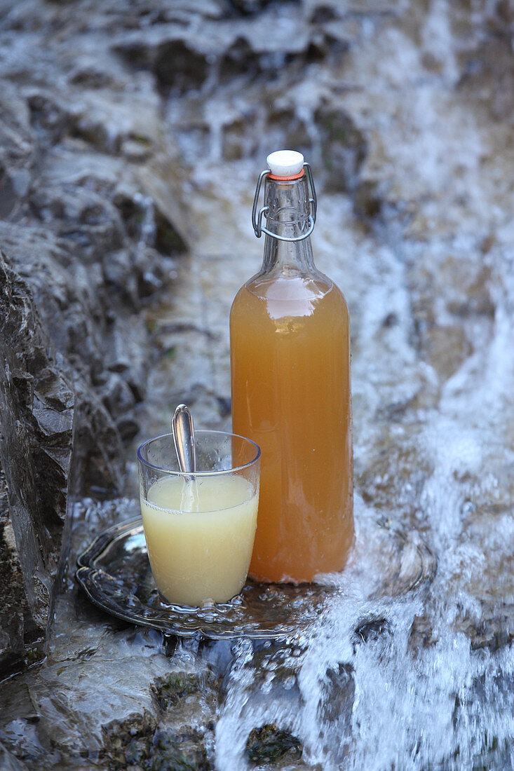 Apple cider vinegar in a bottle and glass, near a natural source of water