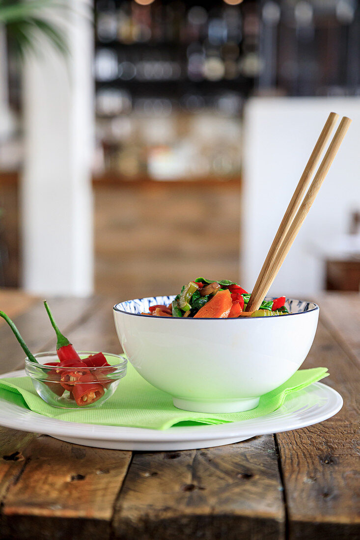 Bowl with appetizing salad and chopsticks, served with red chili pepper