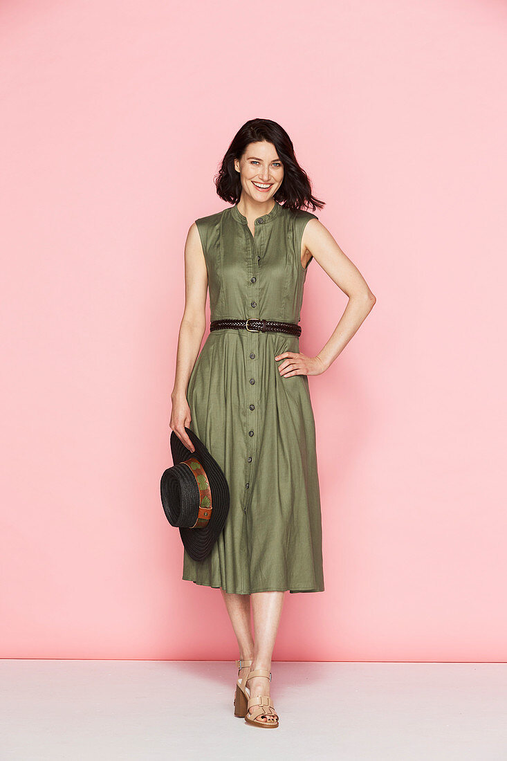 A brunette woman wearing an olive-green summer dress holding a hat