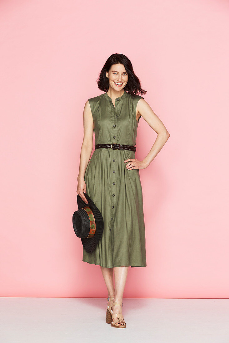Brünette Frau in olivgrünem Sommerkleid und mit Hut in der Hand