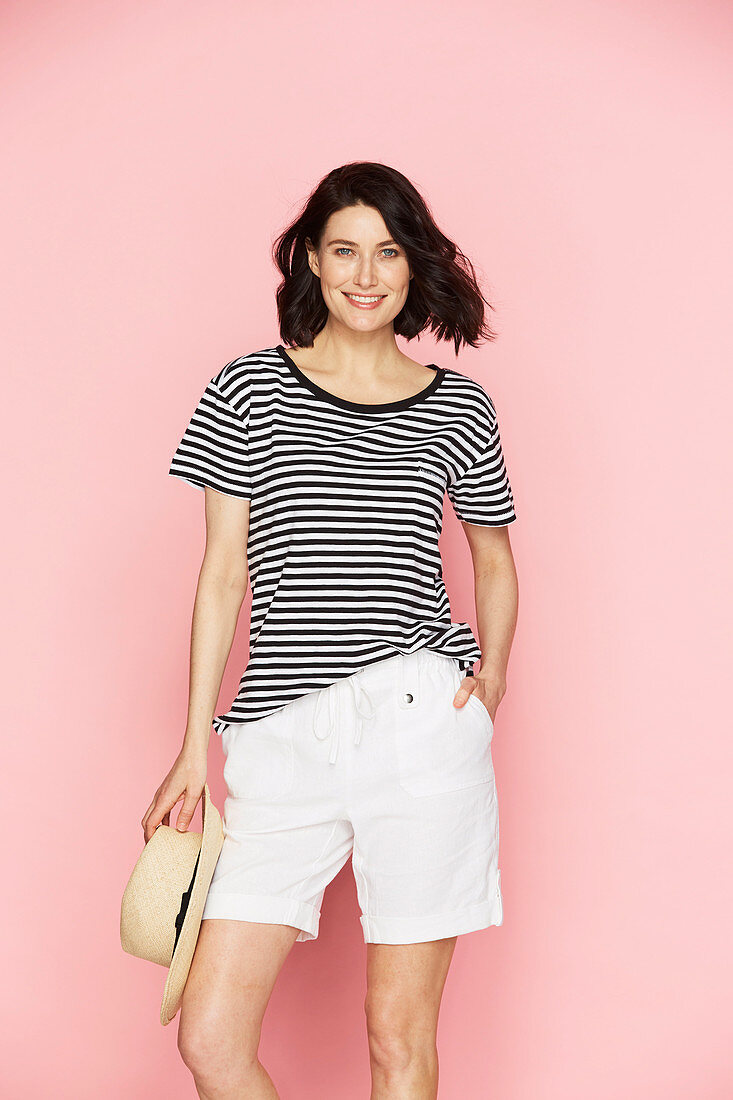 A brunette woman wearing a straw hat, a striped t-shirt and white shorts