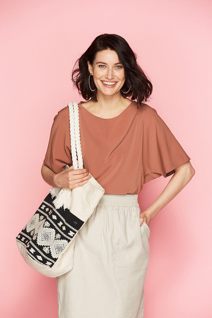 A brunette woman wearing a red-brown blouse and a light skirt