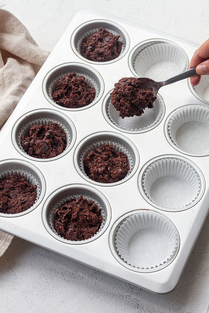 Putting chocolate muffin dough into muffin case on baking pan