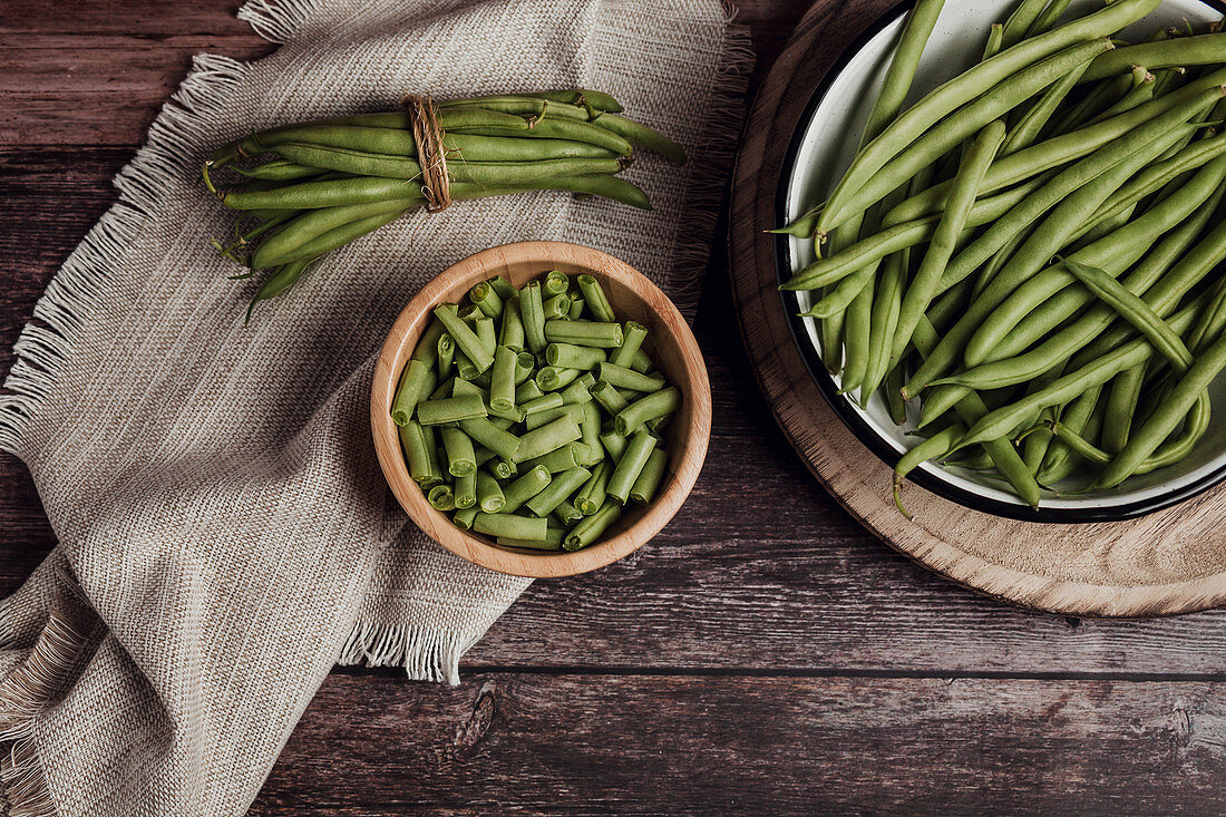 Fresh whole and cut green beans in wooden and metal bowls