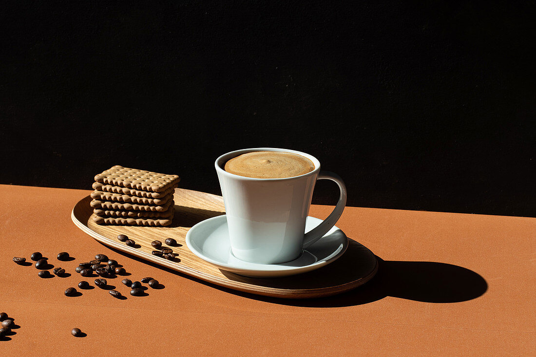 Ceramic cup of tasty coffee and crunchy crackers on wooden plate