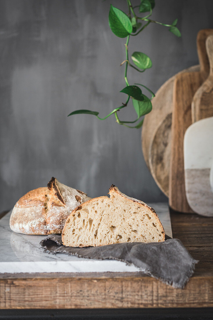 Cut loaf of fresh baked bread with crispy crust on marble tabletop