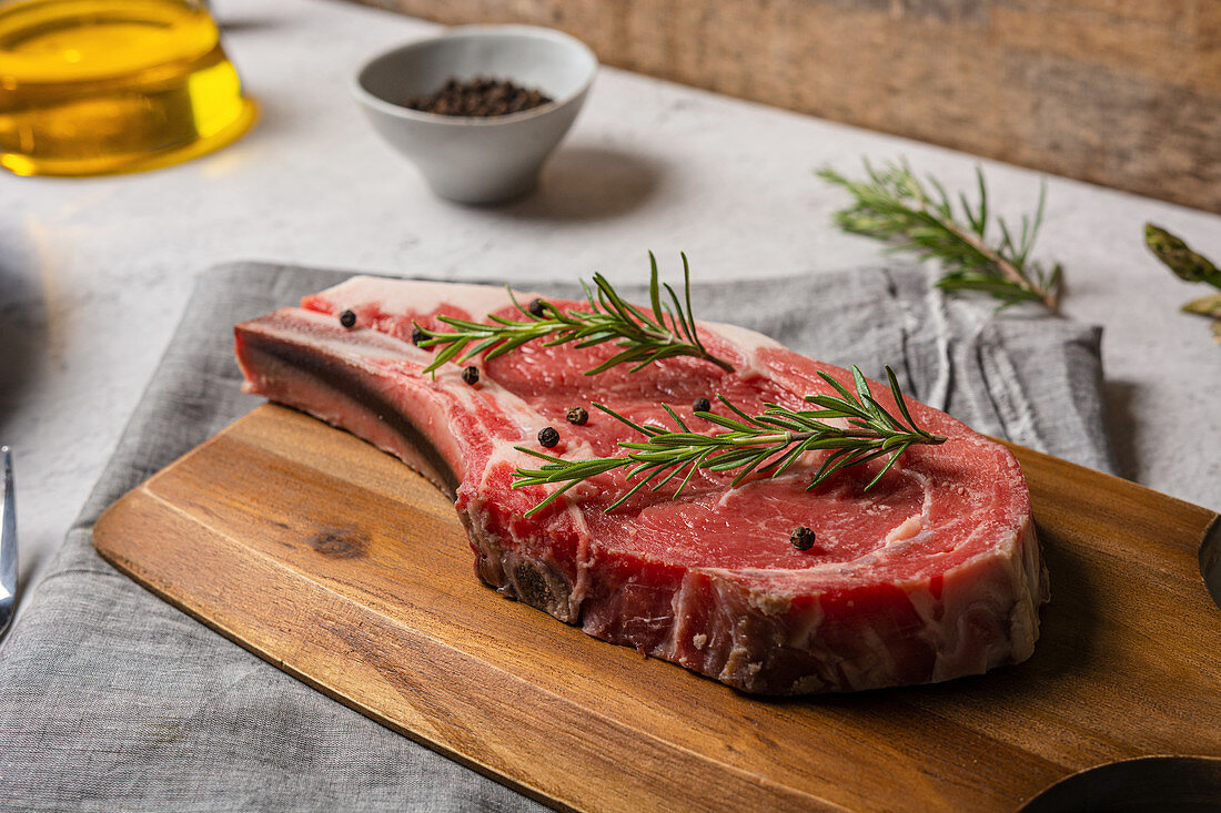 Rohes T-Bone-Steak mit schwarzem Pfeffer und Rosmarin