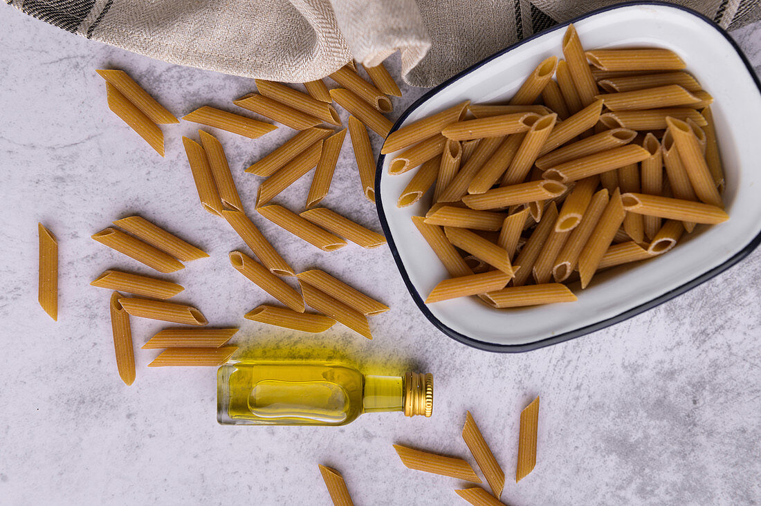 Penne pasta in metal bowl and bottle of virgin olive oil