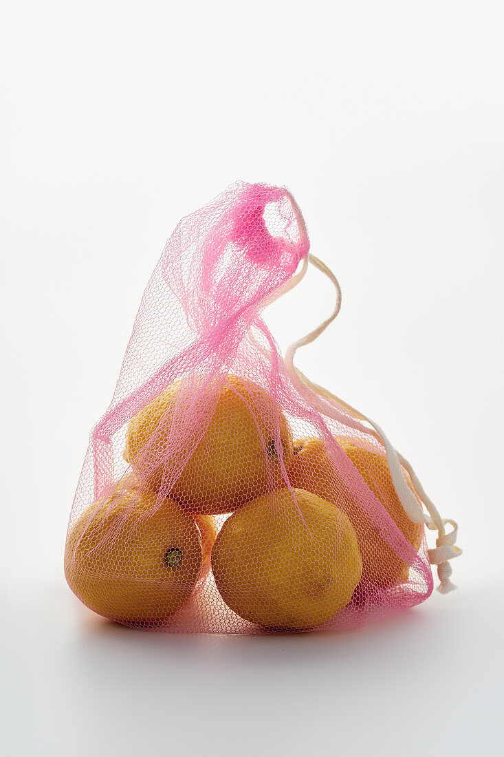 Lemons in pink net textile bag on white background