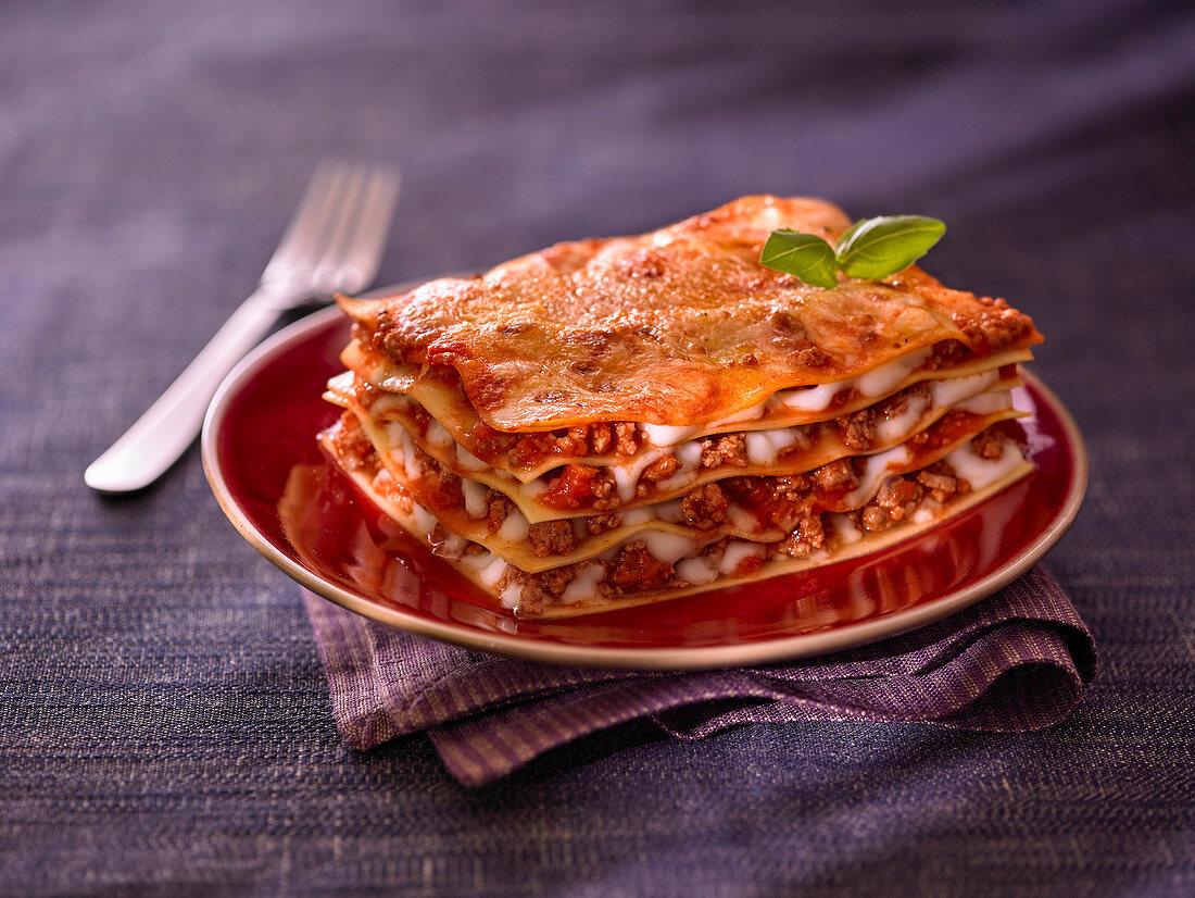 A piece of classic lasagne with a basil leaf