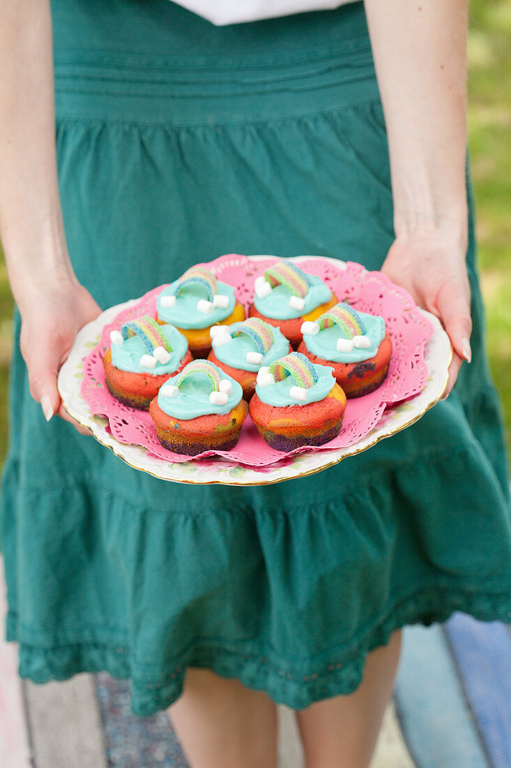 Woman holding a plate with colorful muffins with rainbow decoration
