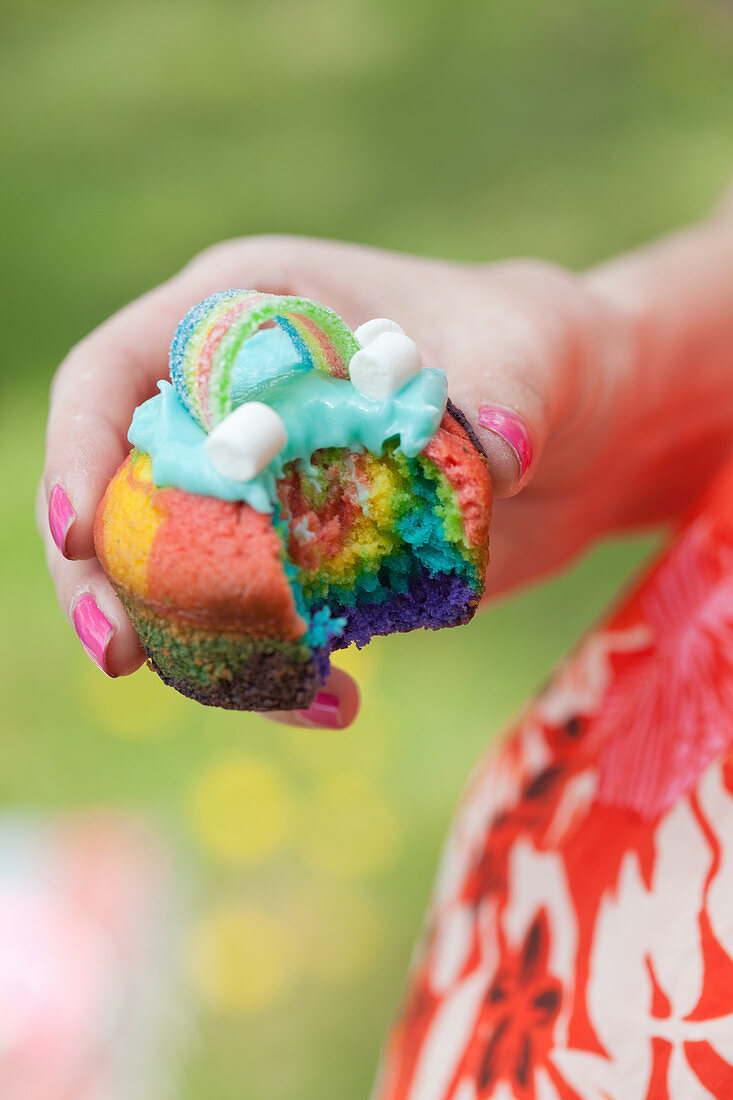 Frau hält angebissenen bunten Muffin mit Regenbogen-Deko