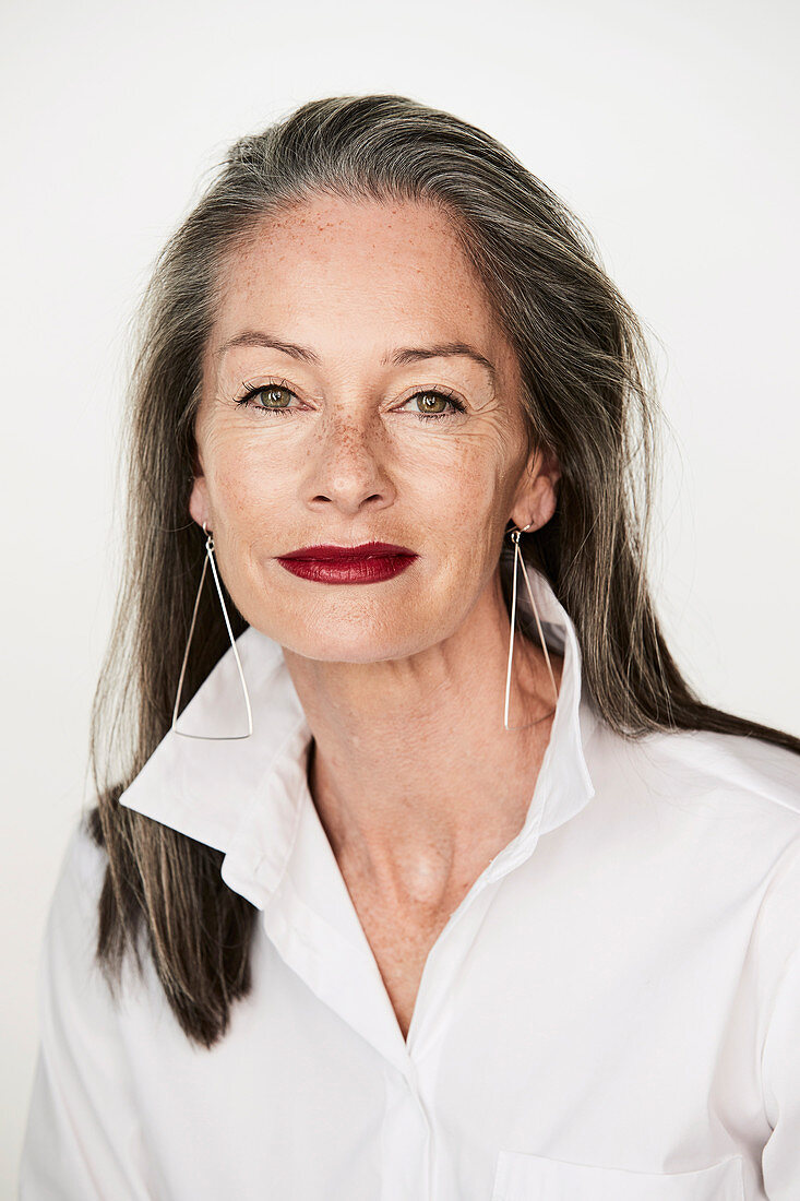 A woman with salt-and-pepper hair wearing earrings and a white shirt