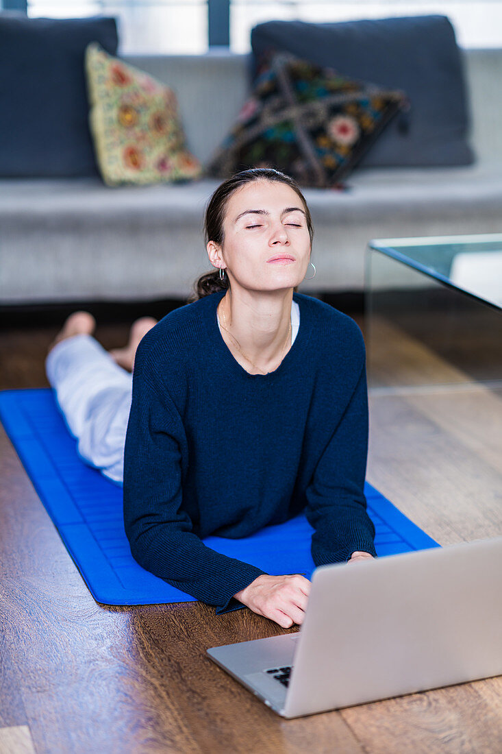 Woman practicing yoga online at laptop at home