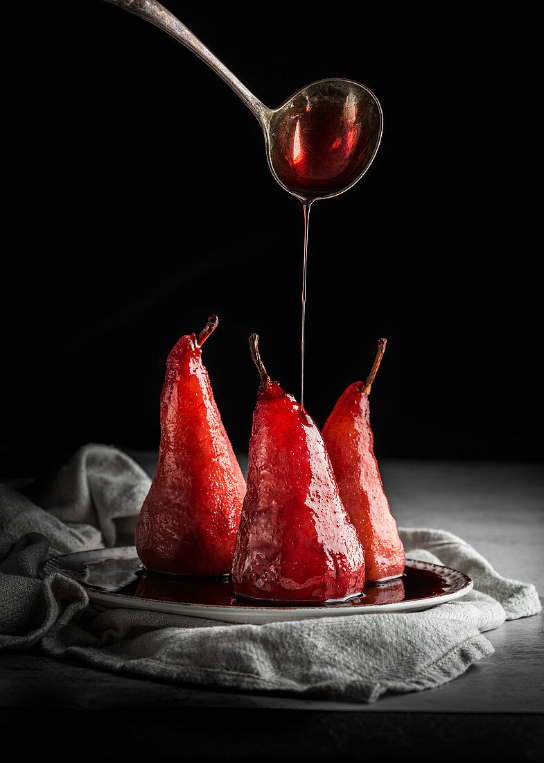 Poached Pear in red wine with red wine pouring from a ladle