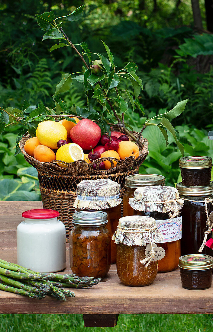 Verschiedene Konservengläser, frisches Obst und grüner Spargel auf Gartentisch