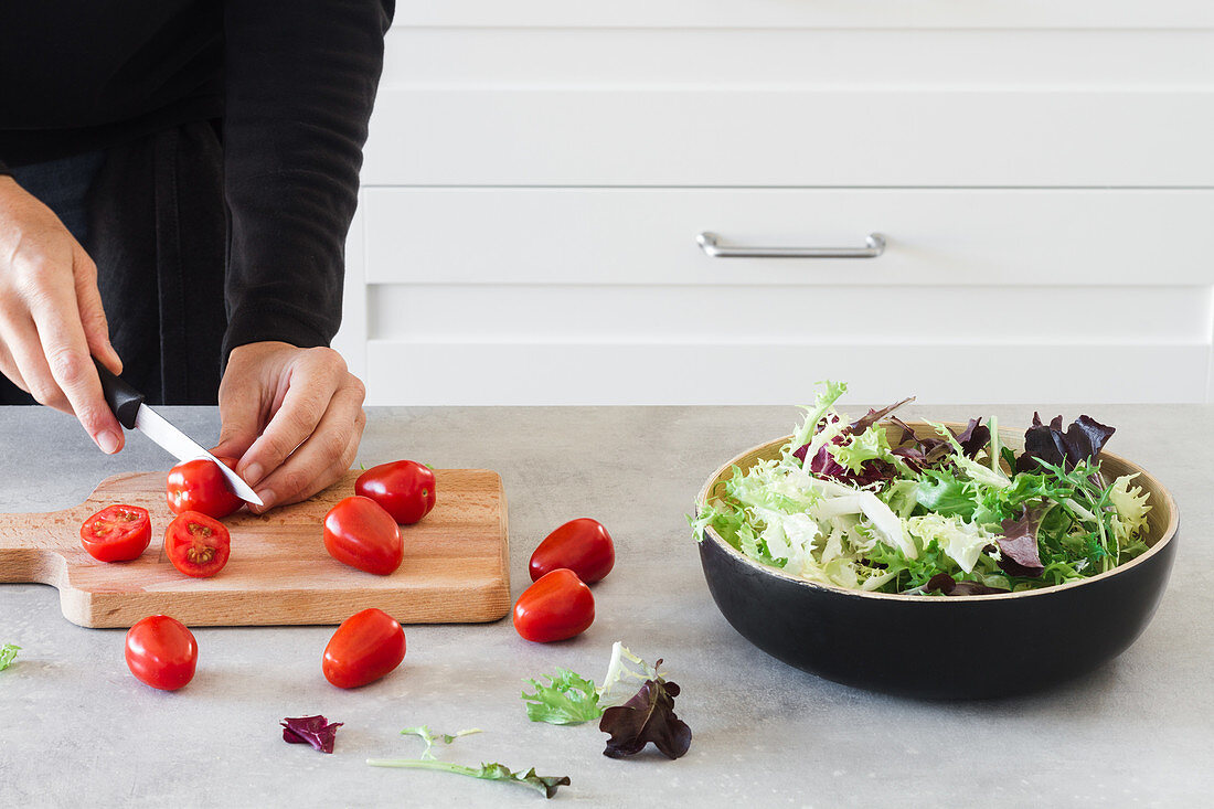 Cutting cherry tomatoes on wooden board for Caesar salad