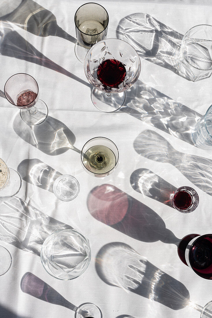 Different glasses with casting shadows and flares on white table