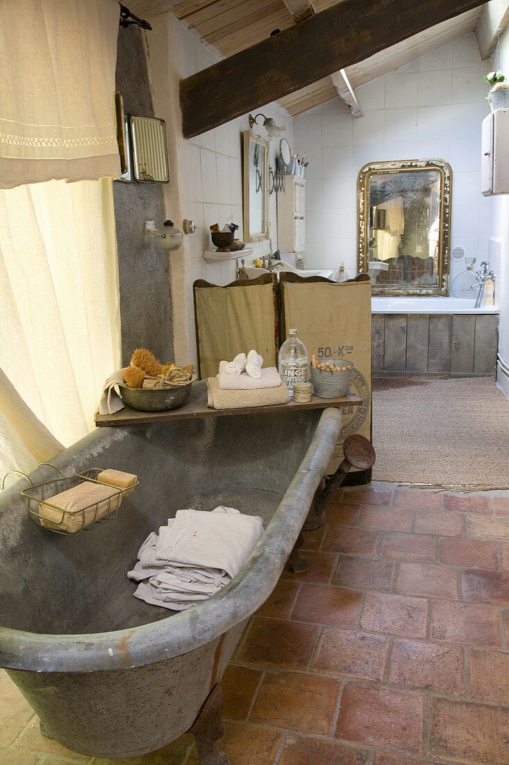 Old metal clawfoot tub in the bathroom with terracotta tile floor