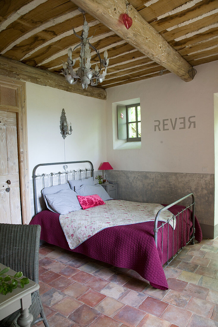 Metal bed in a rustic bedroom with terracotta tile floor