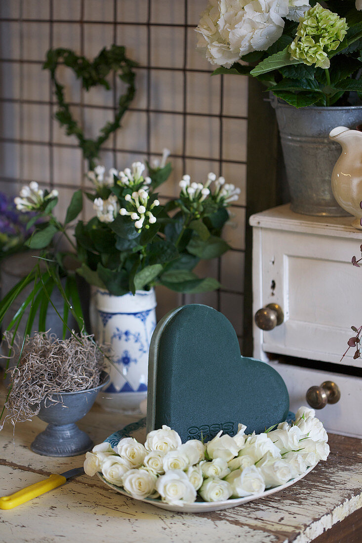 White roses, heart-shaped piece of oasis and vase of bouvardia branches