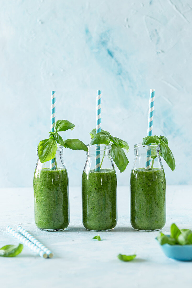 Three green smoothies in glass bottles with straws