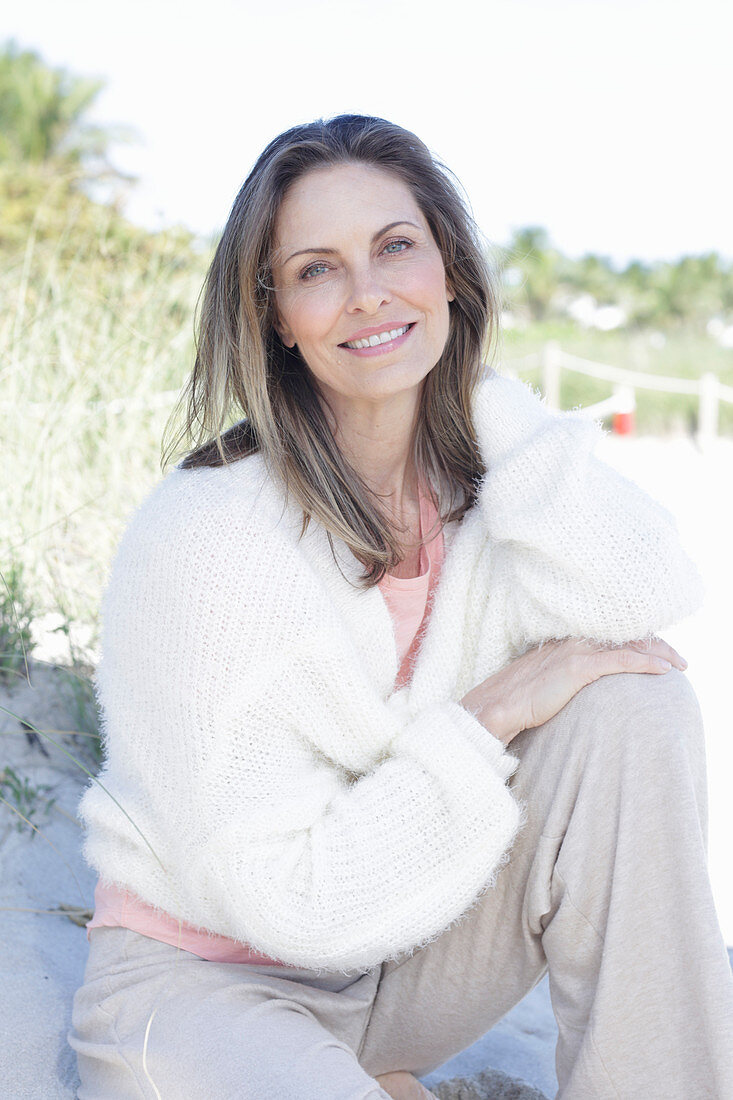 Langhaarige Frau in hellem Pullover und Hose im Sand am Strand