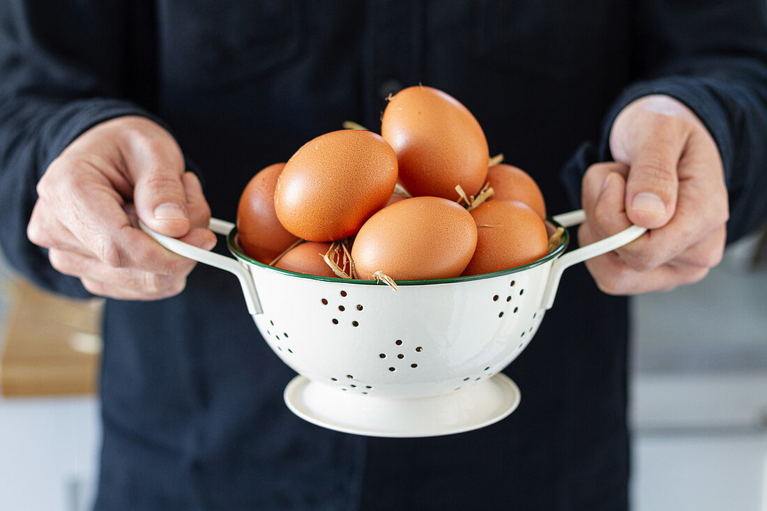 Man holds brown chicken eggs in white colander