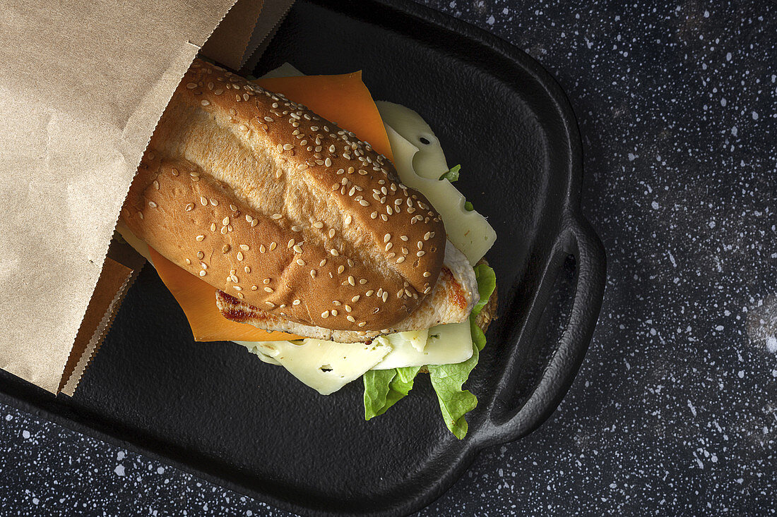 Sandwich with cheese and vegetables in takeaway paper bag