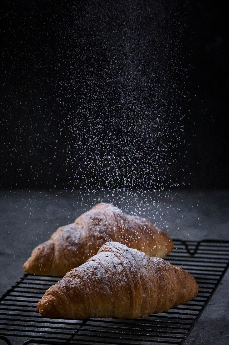 Two croissant with powdered sugar on cooling rack